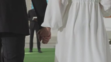 Orta kesimin gerisinde, kimliği belirsiz gelin ve damadın yavaş bir şekilde el ele tutuşup Afrikalı Amerikalı erkek görevliye yaklaşırken kilisede samimi bir düğün töreni düzenlemesi.