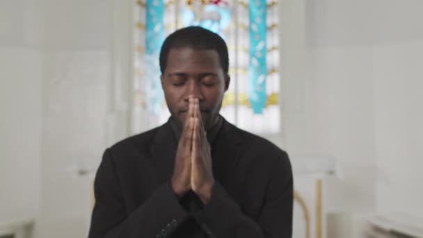 在教堂的蓝色彩色玻璃窗前 年轻的黑人牧师手举着祈祷的手 摆出一副相机的姿势 在慢镜头中 — 图库视频影像