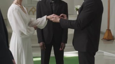 Orta yaşlı, beyaz bir şapelde nikah yüzüklerini taktıktan sonra orta yaşlı, beyaz bir çift olarak ilan eden siyahi erkek memurun orta boy yavaşlığı.