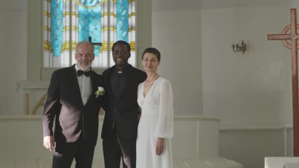 成年白种人新婚夫妇的中肖像画和他们的黑人男官在仪式后站在白色婚礼小礼拜堂拍照 — 图库视频影像