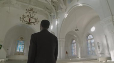 Siyah takım elbiseli Afrikalı Amerikalı erkek rahibin yavaşlaması Lüteriyen kilisesinde mihraba doğru yürüyor.