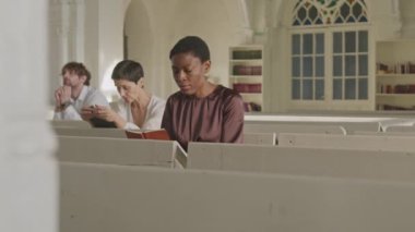 Kilisedeki dini ayin sırasında beyaz ahşap banklarda oturan ve dua eden çeşitli cemaat üyeleri.