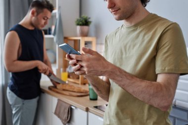 Aynı cinsiyetten çiftlerin yan görüntüsü. Ön planda akıllı telefon kullanan genç adama odaklan. Boşluğu kopyala.