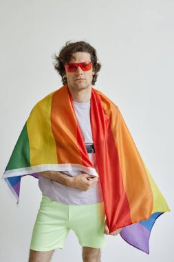 Beyaz arka planda LGBTQ bayrağı takan genç bir gay 'in dikey portresi