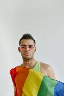 Beyaz arka plana sarılı gurur bayrağına sarılı eşcinsel bir adamın minimum konsept portresi