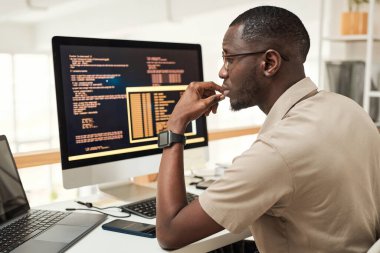 Düşünceli yazılım mühendisi dizüstü bilgisayar ekranında programlama kodunu okuyor