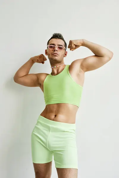 Portrait of muscular non binary man posing against white in studio wearing neon green crop top