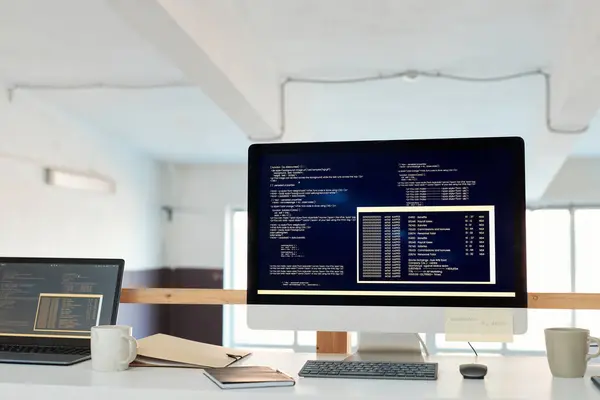 Computer with programming code on screen on office desk of software developer