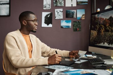 Yaratıcı siyahi adam evde çalışırken bilgisayardaki manzara fotoğraflarını düzenliyor