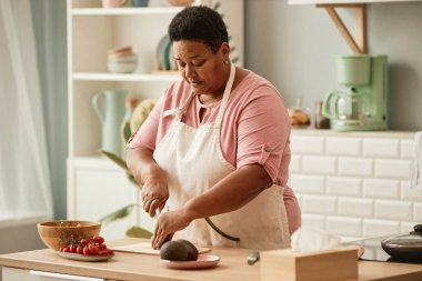 Ev mutfağında yemek pişiren son sınıf siyahi bir kadının sıcak tonlu portresi.