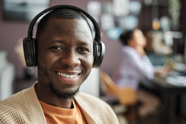 Portra of smiling Black man listening to music in headphones when working in office