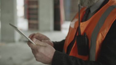 İnşaat alanında dijital tablet kullanan, gri saçlı ve sakallı, kendine güvenen beyaz ustabaşının görüntüsü.