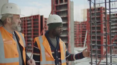 Güvenlik üniformalı iki farklı erkek ustabaşı ve inşaat işçisinin bitirilmemiş alanlarda iş meselelerini tartışırken belini kaldır.