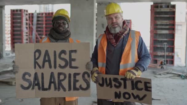 Mittlere Aufnahme Zweier Ethnisch Unterschiedlicher Bauarbeiter Mit Demonstrationsbannern Der Hand — Stockvideo
