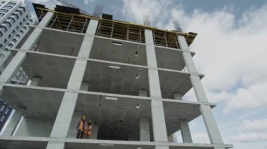 Çok katlı gayrimenkul geliştirme sürecinin düşük açılı çekimi. Güvenlik yelekli iki inşaat mühendisi henüz tamamlanmamış beton blokta tartışıyorlar.
