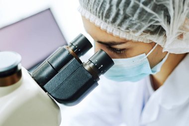 Laboratuvarda tıbbi araştırmalar yaparken mikroskoba bakan genç bir kadın.