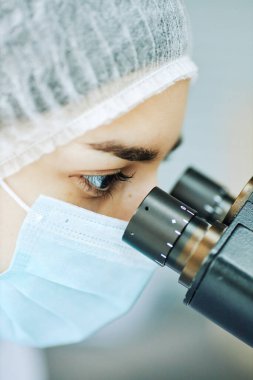 Laboratuvarda test örnekleriyle çalışırken mikroskoba bakan genç kadın doktorların dikey yakın çekimi.