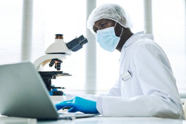 Tıp laboratuarında araştırma yapan ve dizüstü bilgisayar kullanan siyah bir adamın yan görüş portresi.