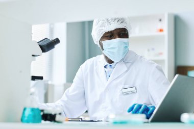 Laboratuvarda bilimsel araştırma yapan ve maske takan siyahi bir adamın portresi.