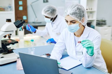 Modern laboratuarda çalışan ve kan testleri yapan Orta Doğulu genç bir kadının portresi.