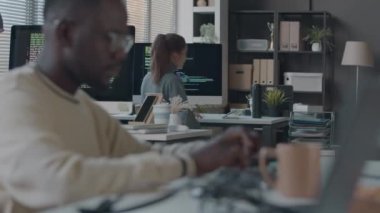 Genç beyaz kadın programcının bilgisayardaki kodlamayı bitirdiği, iş yerinden kalkıp siyahi erkek meslektaşıyla konuştuğu, modern ofiste birlikte çalıştığı orta boy bir fotoğraf.