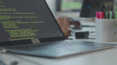 Modern ofisteki siyah dizüstü bilgisayarda görünen yeşil HTML kodlarının yakın plan görüntüsü. Tanımlanamayan programcı bulanık arkaplanda çalışıyor.
