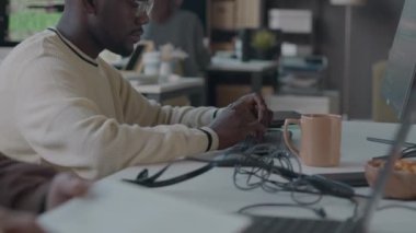 Modern programcılar ofisinde iş arkadaşlarıyla birlikte çalışırken kablosuz klavyede yazan genç siyahi erkek yazılım geliştiricisinin belini kaldırın