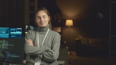 Akşamları elleri koyu programcıların ofisinde katlanmış kameraya poz veren Kafkas kadın bilişim koordinatörünün orta yavaş portresi.