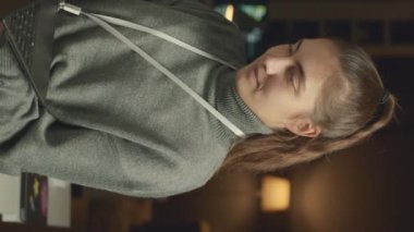 Geceleri karanlıkta tek başına çalışırken kameraya dizüstü bilgisayarla poz veren beyaz kadın programcının dikey portresi.