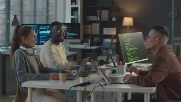 現代のオフィスの1つのテーブルに座って コンピュータ上で話し コーディングするプログラマの民族的に多様なチームのミディアムショット — ストック動画