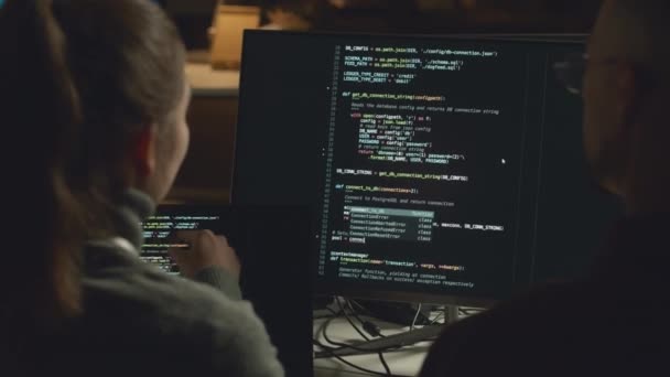 夜に一緒にプログラマオフィスで働いている間 デスクトップコンピュータでプログラムコードを議論する男女のバックビューチェストアップ — ストック動画
