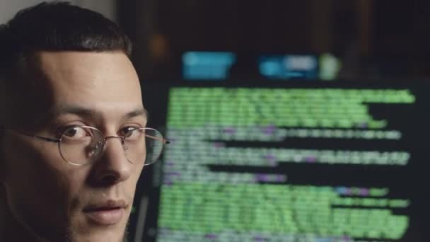 夜のオフィスのデスクトップコンピュータでプログラムコーディングしながら 眼鏡の若いBiracial男性プログラマーのミディアムクローズアップポートレート — ストック動画