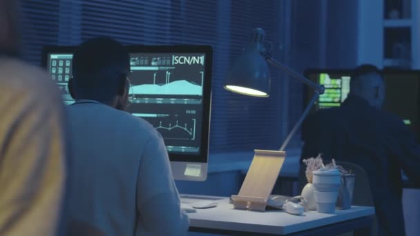 夜の青いネオン照明でダークオフィスで働いている間 パーソナルコンピュータ上のデータを監視するサイバーセキュリティワーカーのプロチームのバックビューショット — ストック動画