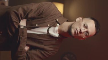 Tespih, kolye, bilezik ve gözlük takan ve elleri kapalı kameraya poz veren kendine güvenen genç bir çift cinsiyetli adamın portresi dikey.