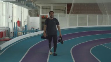 Kafkas esmer, sakallı, bacak protezi takan spor çantalı ve koşu bıçağıyla antrenman için kapalı stadyuma varan ve güvenli bir şekilde yürüyen bir sporcu.