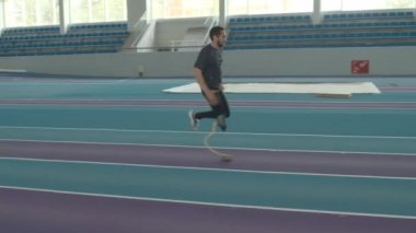 Engelli, atletik, genç, beyaz bir adam, kapalı stadyum boyunca neşterle koşuyor.