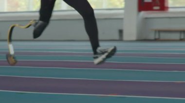 Düşük çözünürlüklü yavaş çekim. Kapalı alanda koşan, tanınmayan, protez bacaklı bir erkek sporcu.