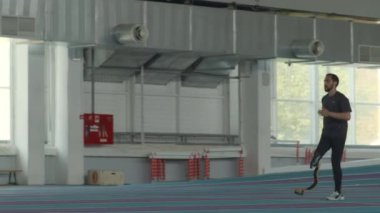 Protez uzuv eğitimi almış beyaz erkek sporcunun stadyumdaki kapalı pistte koşuşunu çekiyoruz.