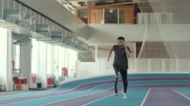 Ampüte edilmiş bacağında koşu bıçağı olan profesyonel sporcunun yavaşı kapalı stadyumda koşu yolunda koşuyor.