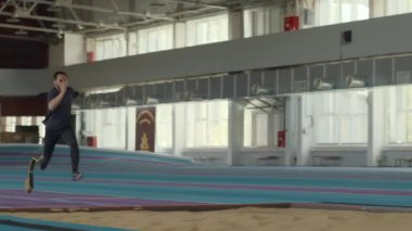 Beyaz tenli, protez koşu bıçaklı bir sporcu uzun atlama yaptıktan sonra raydan çıkıyor.