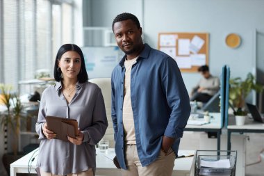 Ofiste dikilirken kameraya gülümseyen iki etnik gencin belini kaldırın.