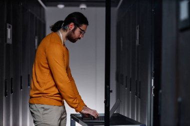 Sunucu odasında dizüstü bilgisayar kullanan sakallı ağ mühendisinin minimal yan görünüm portresi