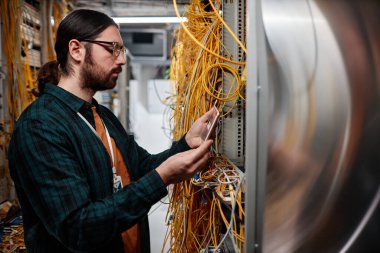 Sunucu ayarlayan ve akıllı telefon kullanan sakallı sistem yöneticisinin yan görünüm portresi