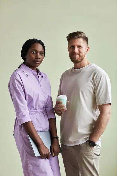 Minimal portrait of two young business people, man and woman looking at camera against pastel green wall