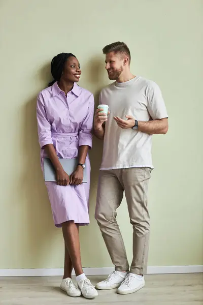 Minimal full length portrait of two young people, man and woman smiling against pastel green wall