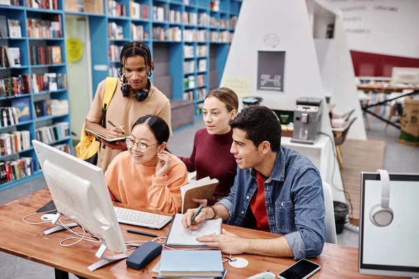 Diverse group of college students using computer together in colorful library interior and enjoying studying