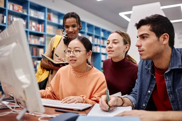 Diverse group of college students in library, focus on Asian girl using computer with friends