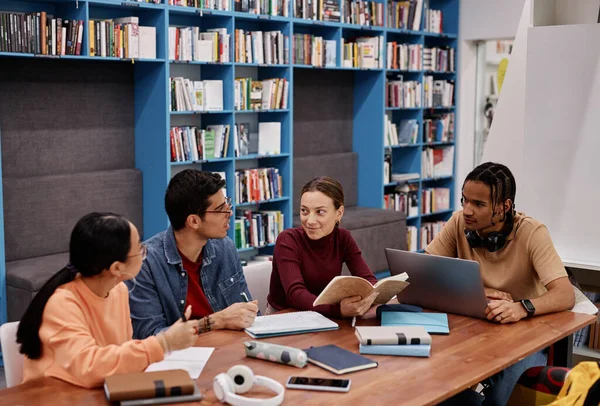 Diverse group of young people studying together sitting at table in modern college library
