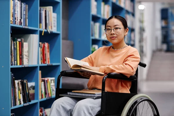 Portrait of Asian young woman with disability in library setting at modern college smiling at camera