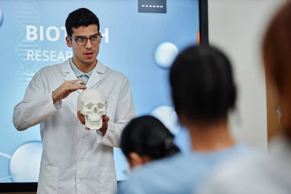 Waist up portrait of doctor holding skull model during lecture or seminar in med college, explaining bone structure and brain surgery methods